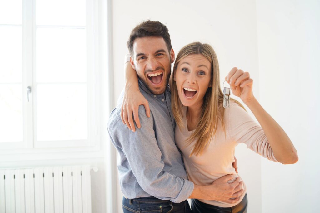 Excited young couple smiling and hugging. The woman is holding up keys in her hand